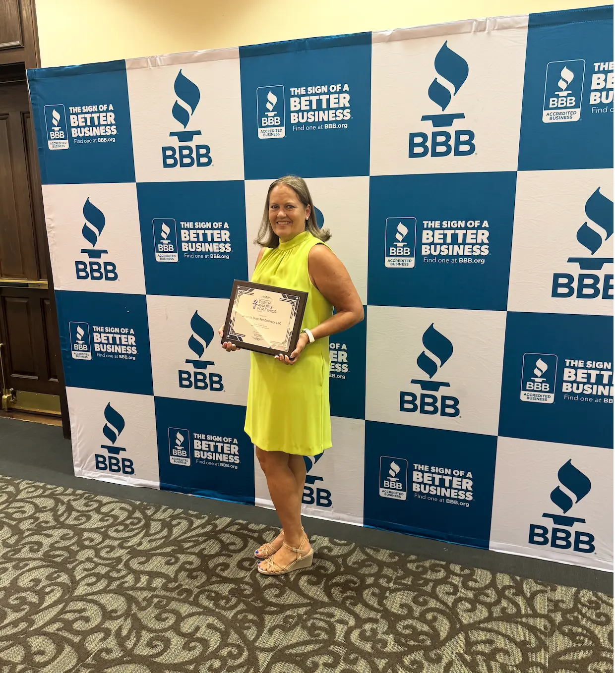Rachel Carey holding the Better Business Bureau Torch Awards for Ethics honoree plaque in front of the BBB backdrop